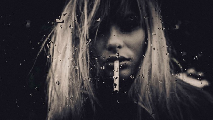 Monochrome portrait of a woman smoking through raindrops