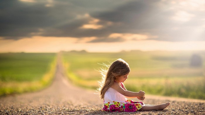 Little girl sitting on a dirt road at sunset