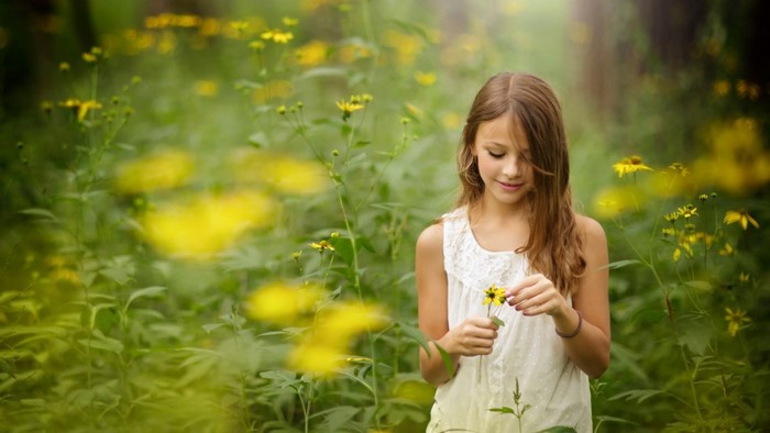 Young girl in a white dress holding a yellow flower in a meadow