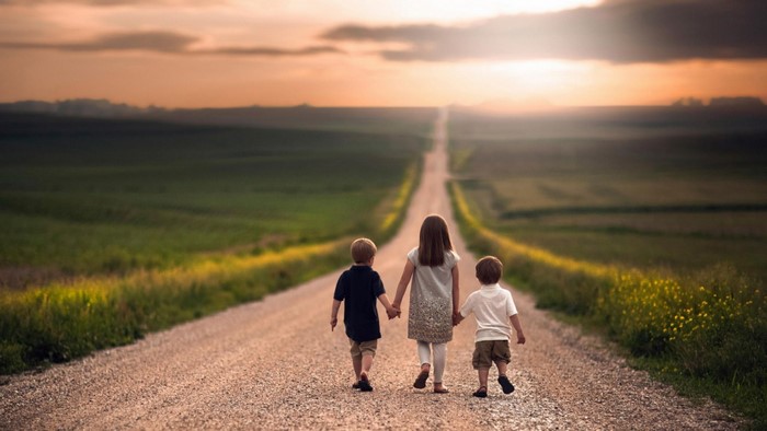 Three children walking on a dirt road at sunset