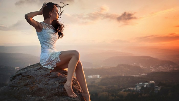 Woman Sitting on Rock at Sunset with Flowing Hair