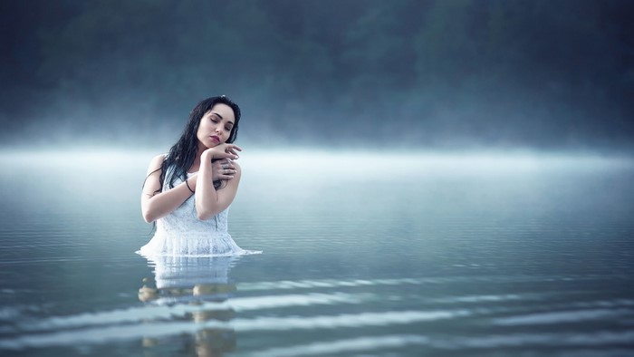 Woman in white dress standing in a misty lake