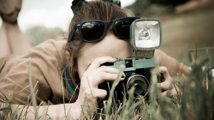 Woman with sunglasses taking a photo with a vintage camera