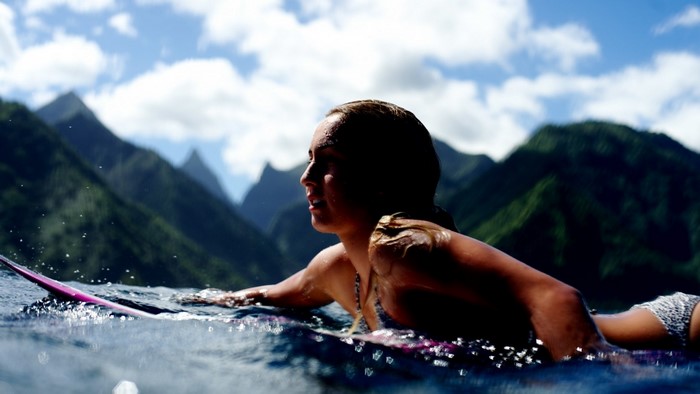 Woman surfing in the ocean with mountains in the background