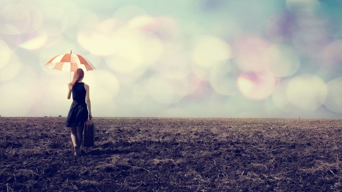 Woman with umbrella and suitcase in a field