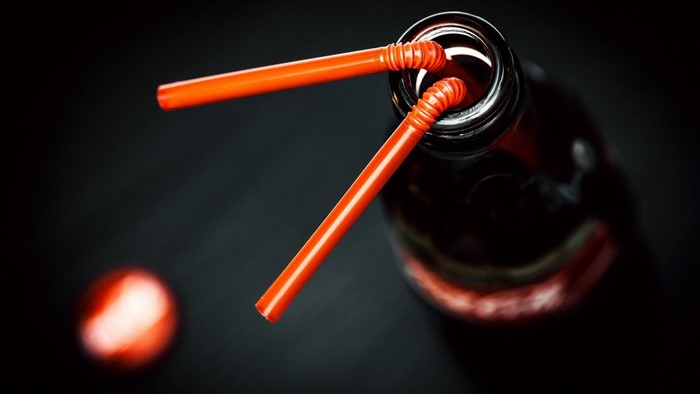 Two orange straws in a dark bottle of Coca-Cola