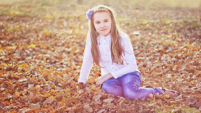 Girl with flower in hair sitting in autumn leaves