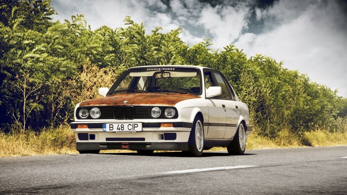 White BMW E30 sedan with rusty hood on a road