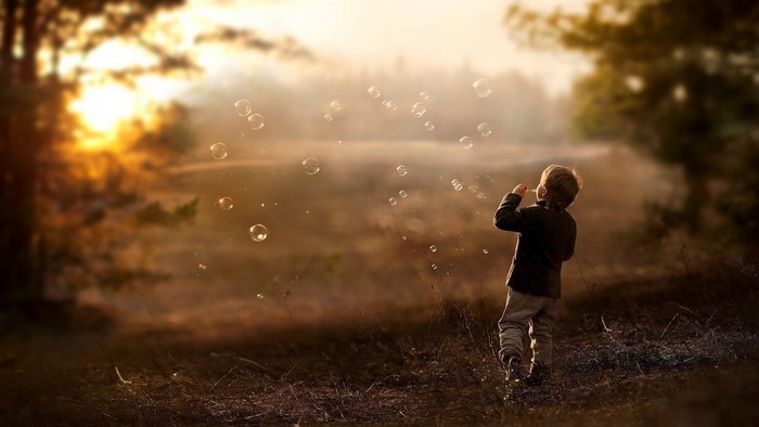 Boy blowing bubbles at sunset in a field