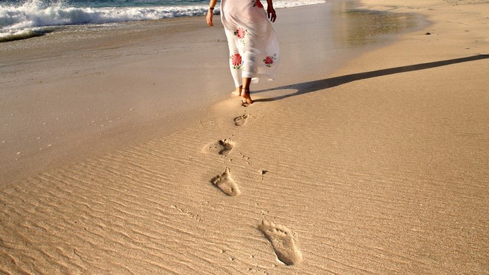 Person walking on a sandy beach leaving footprints