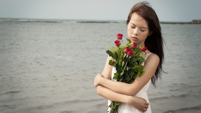 Young woman holding a bouquet of red roses on the beach