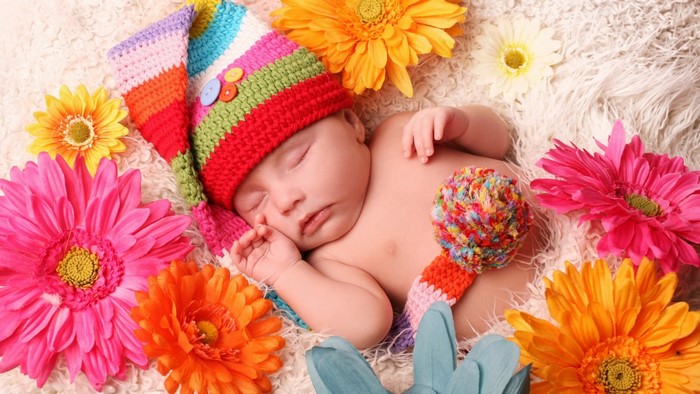 Baby in colorful hat surrounded by flowers