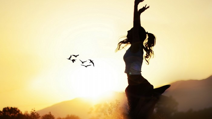 Silhouette of a woman jumping at sunset with birds flying