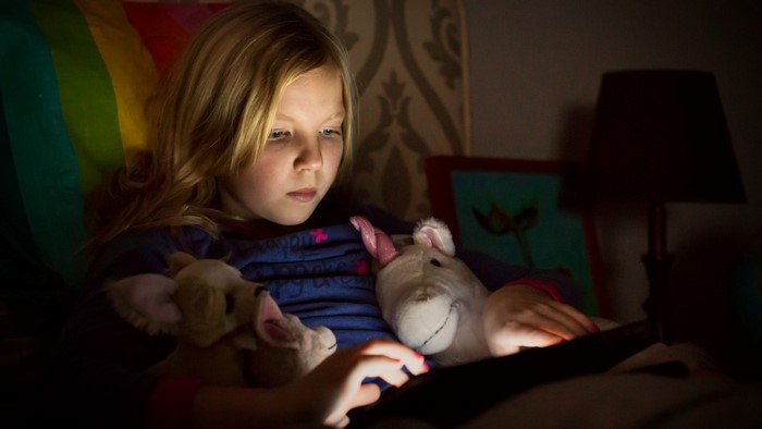 Young girl reading on a tablet with stuffed animals