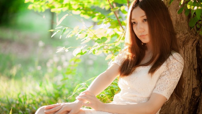 Young woman in white dress sitting by a tree