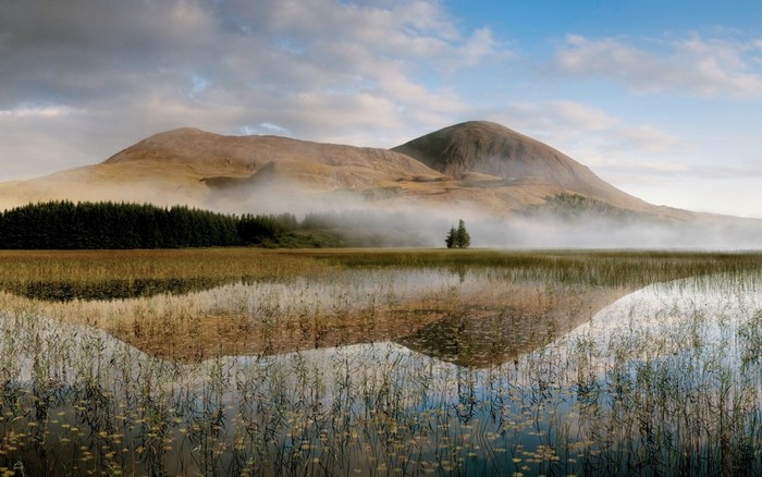 Misty mountains reflected in a calm lake at dawn