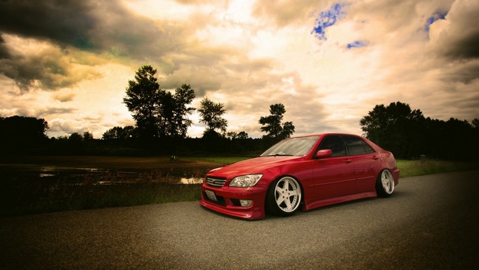 Red sports car parked on a road with trees and clouds