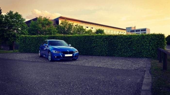 Blue BMW parked in front of a building and hedge