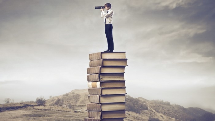 Man with telescope standing on stack of books