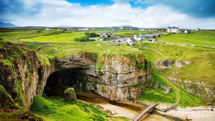 Coastal cave with a village on the green hills above