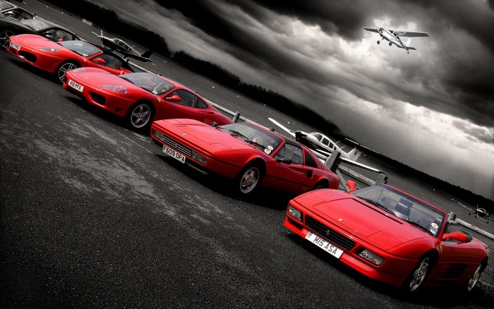 Red Ferraris and a small airplane on a runway