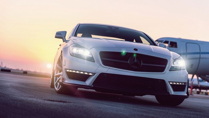 White Mercedes-Benz CLS parked near a private jet at sunset