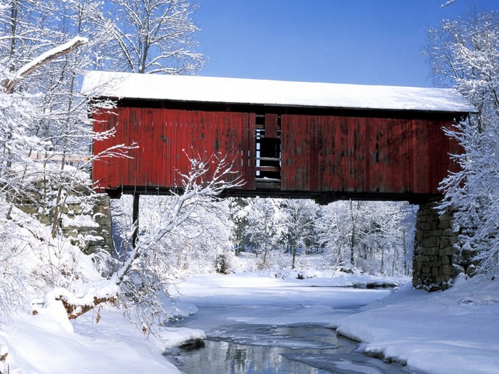 Red covered bridge over a frozen river in winter