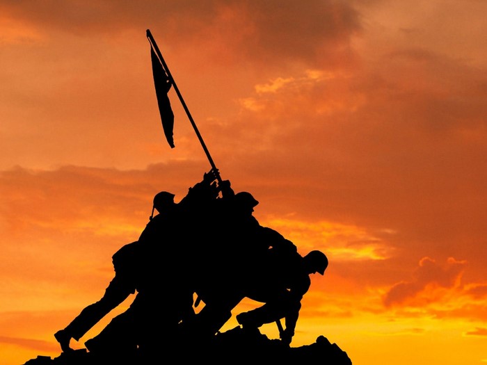 Silhouette of soldiers raising a flag at sunset