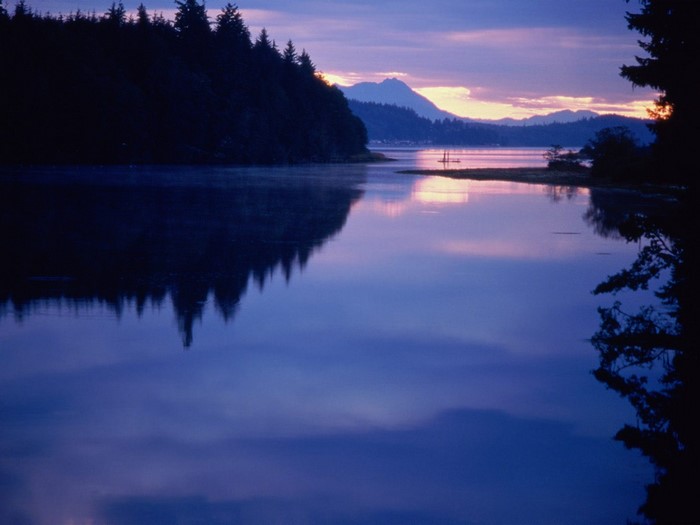 Calm lake reflecting trees and mountains at sunset