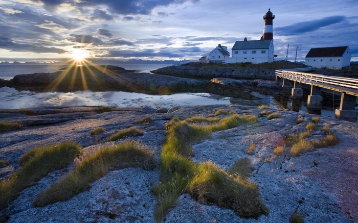 Lighthouse and buildings on a rocky coast at sunset
