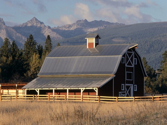 Red barn with metal roof and wooden fence in front of mountains