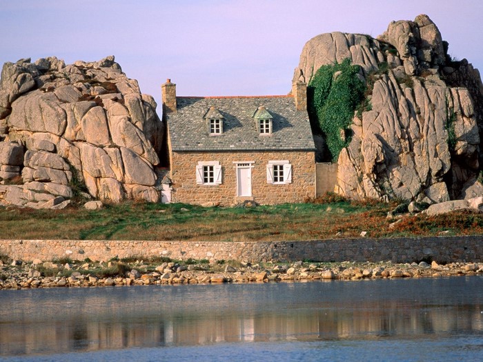 Stone house nestled between large rocks by the water
