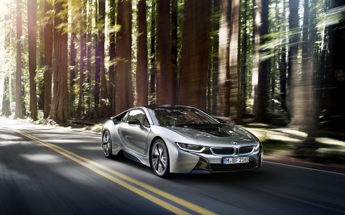 Silver BMW i8 driving on a road through a forest