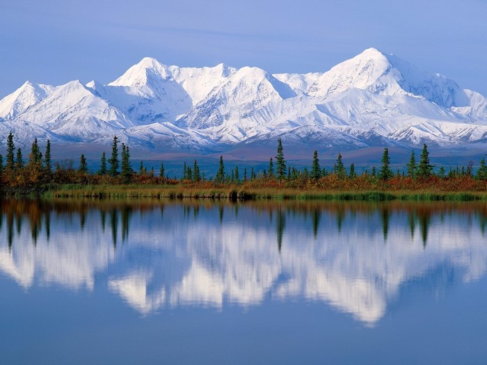 Snow-capped mountains reflected in a calm lake with evergreen trees