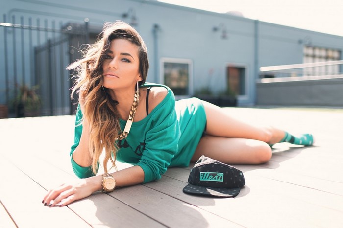 Woman in teal sweatshirt lying on deck with hat