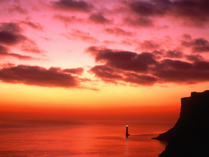 Sunset over the sea with a lighthouse and cliff