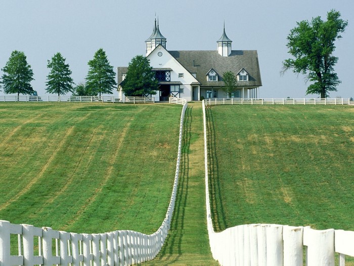 White fence leading to a large white building on a grassy hill