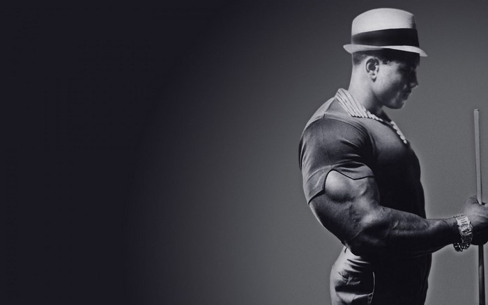Sergio Oliva, bodybuilder, wearing a hat and holding a pool cue