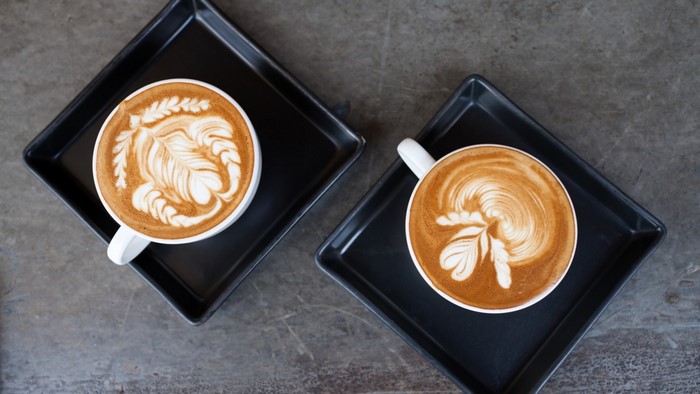Two cups of latte art coffee on black trays