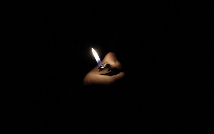 Hand holding a lit lighter in the dark