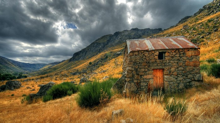 Stone cabin in a mountain valley with dramatic clouds