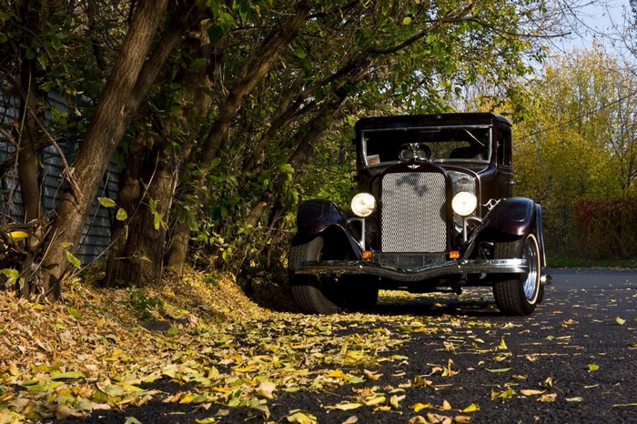 Vintage car parked on a road with autumn leaves
