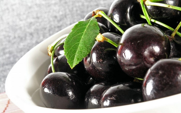 Close-up of dark cherries in a white bowl with a leaf