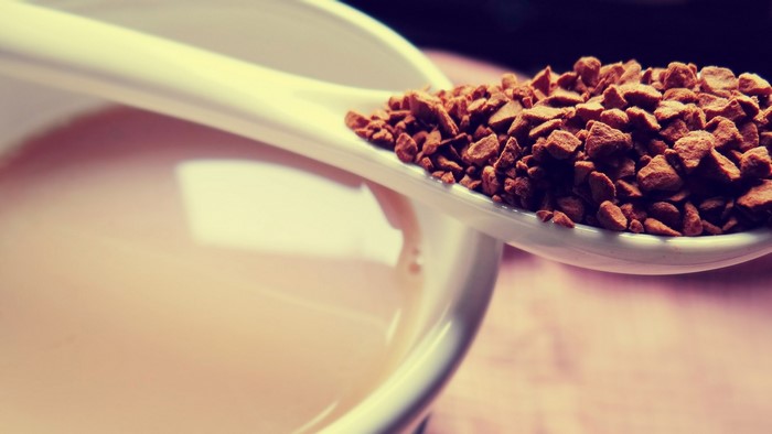Spoonful of instant coffee granules over a cup of coffee