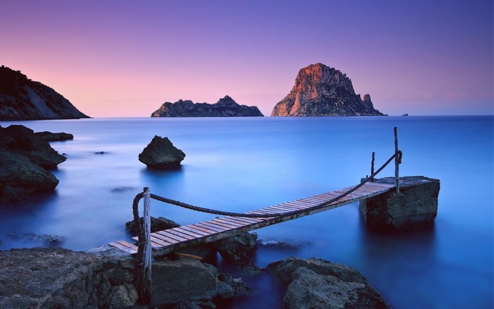 Wooden pier extending into the sea with islands at sunset