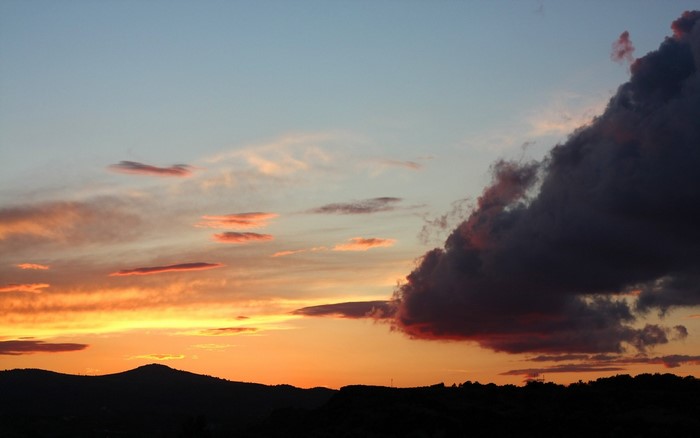 Sunset over a silhouetted landscape with dramatic clouds