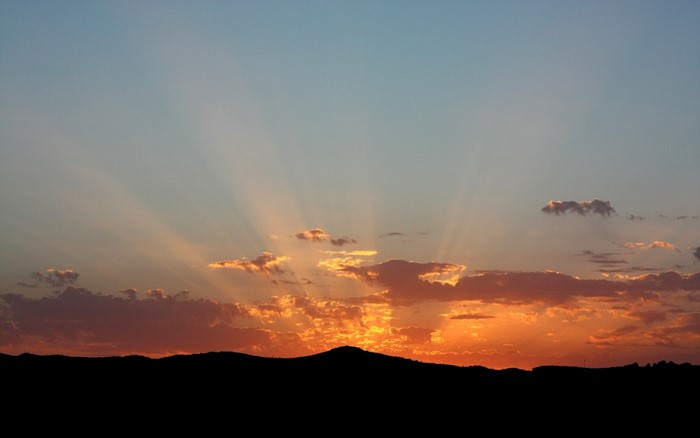Sunset with crepuscular rays over a silhouetted landscape