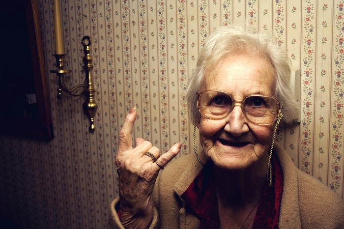 Elderly woman with glasses making rock on gesture