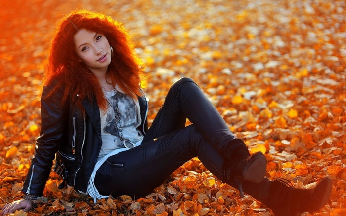 Young woman with red hair sitting in autumn leaves