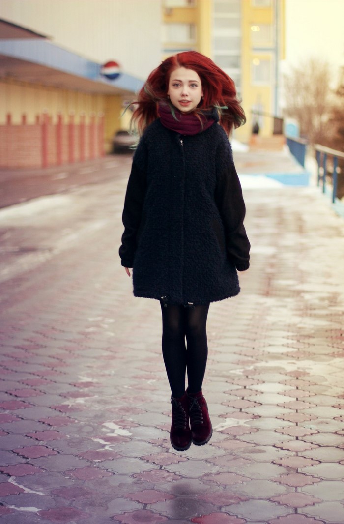 Woman with red hair jumping in a dark coat